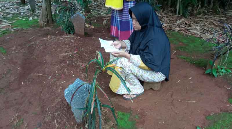 Seorang Wanita membaca buku yasin di atas makam suaminya